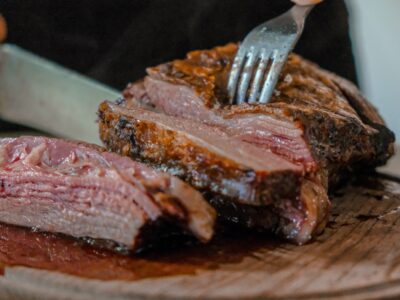 person slicing a meat on brown wooden board